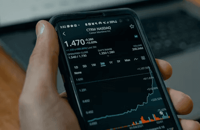 Person holding a phone showing trading charts